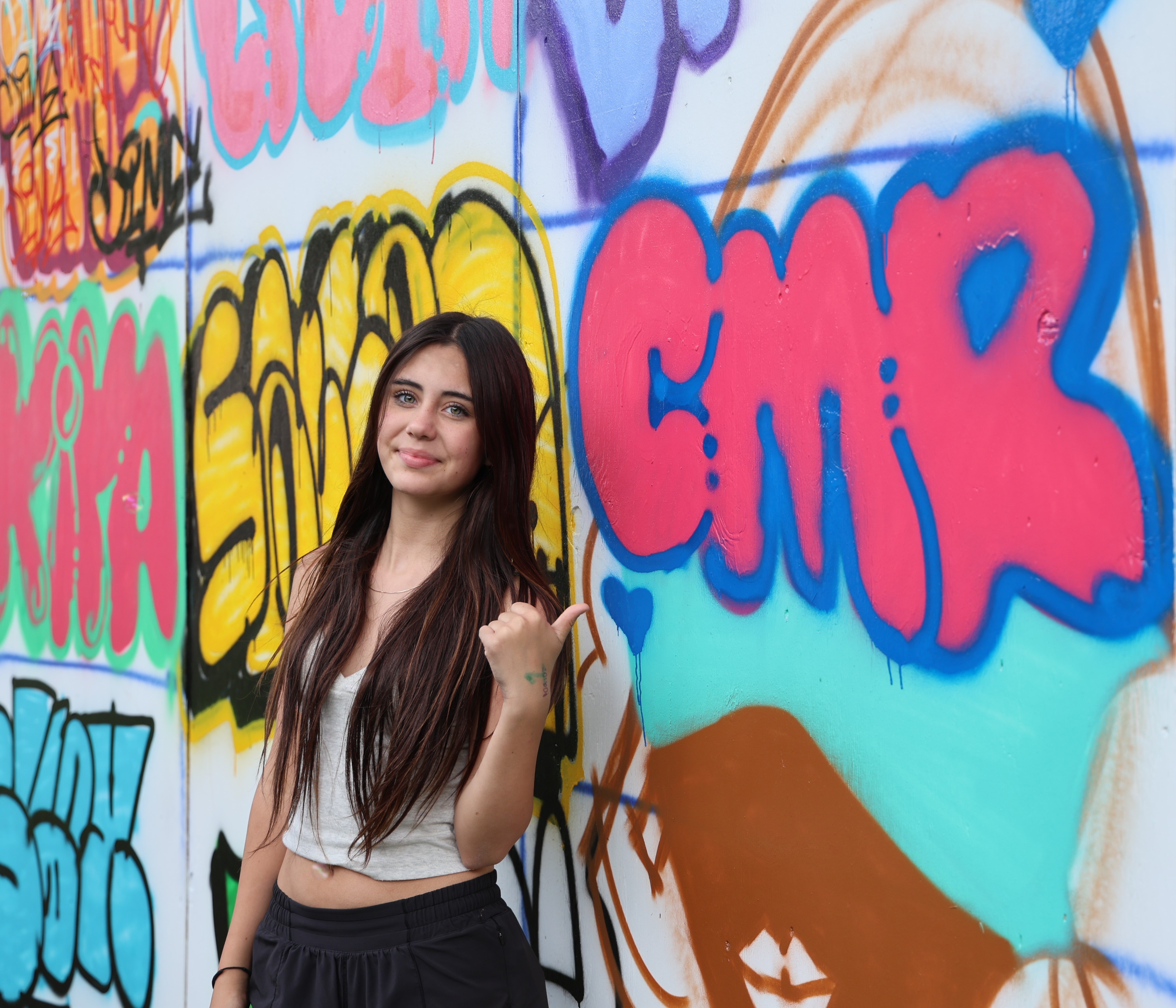 Teenager gives a thumbs-up gesture in front of a graffiti wall.